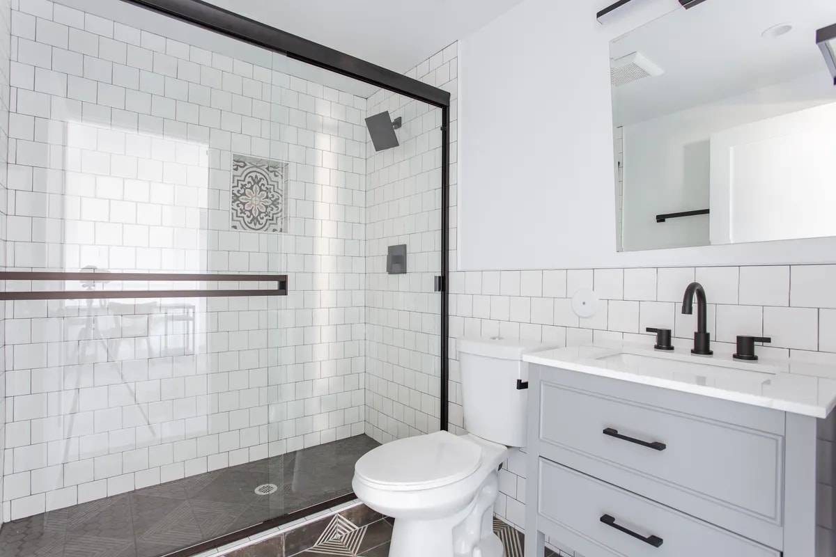 Private bathroom with a glass walk-in shower, black rain showerhead, white subway tile with a patterned tile niche, and a grey vanity with black fixtures