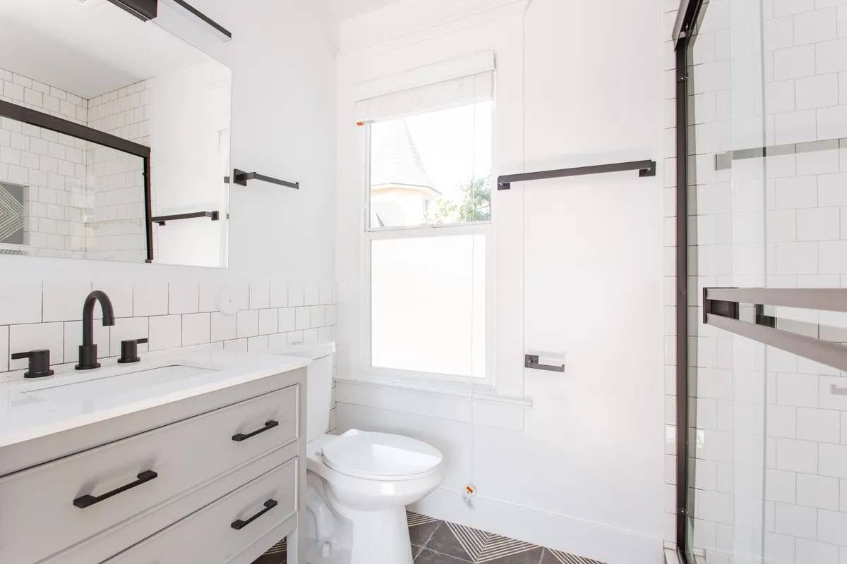 Bathroom with a window, a grey vanity with black faucet, white subway tile and geometric patterned floor tile