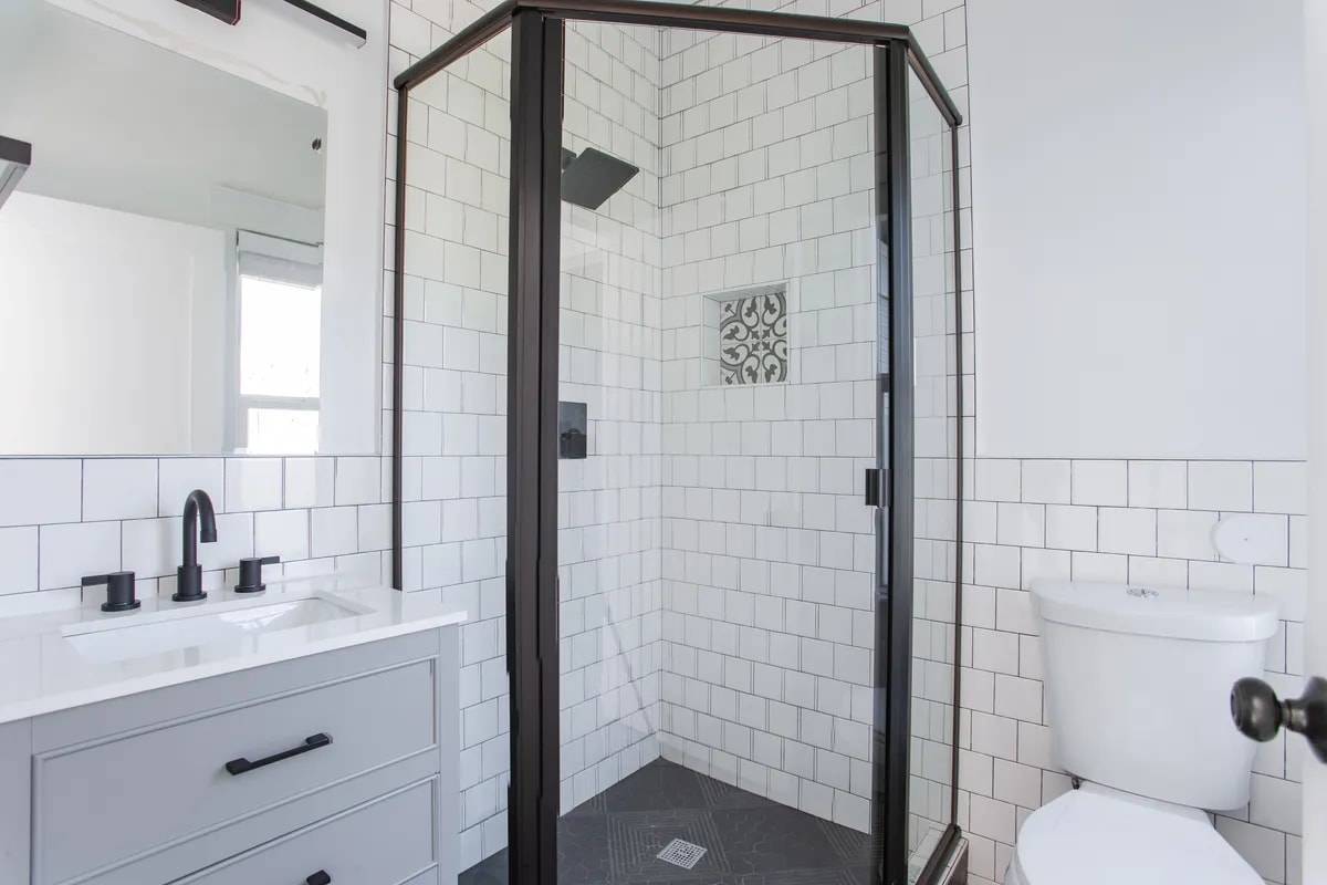 Bathroom with a black-framed corner glass shower, a patterned tile niche and a grey vanity