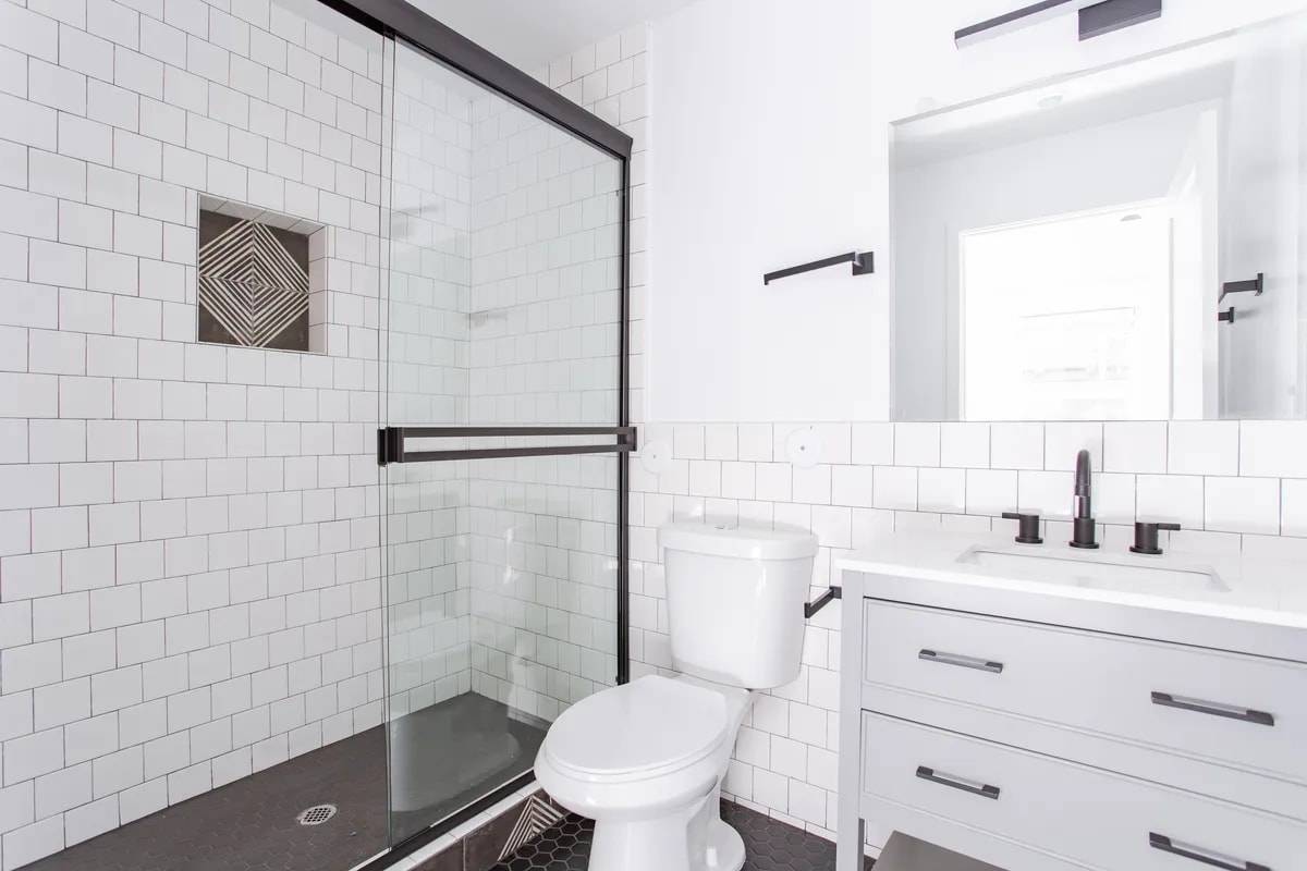 Bathroom with a sliding glass shower door, white subway tile with a diamond-pattern niche, and a grey vanity with black fixtures