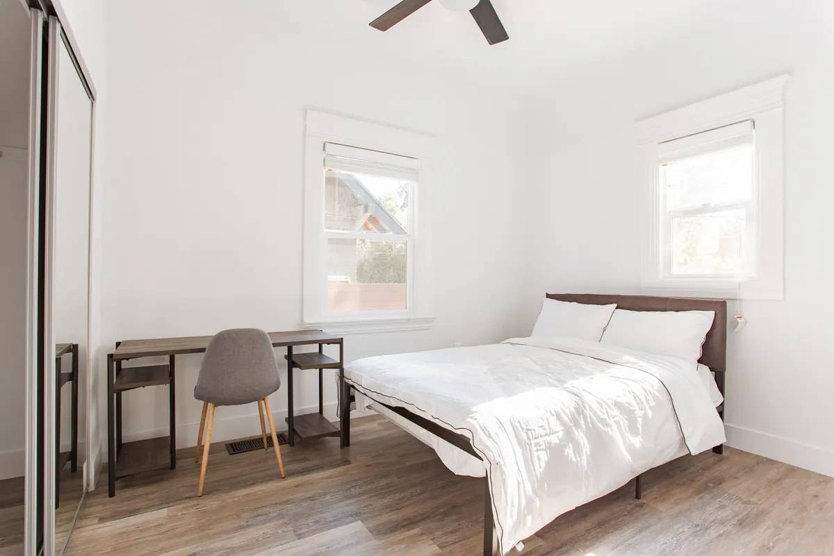 Bedroom with two windows, a mirrored sliding closet, a desk and a bed with white bedding