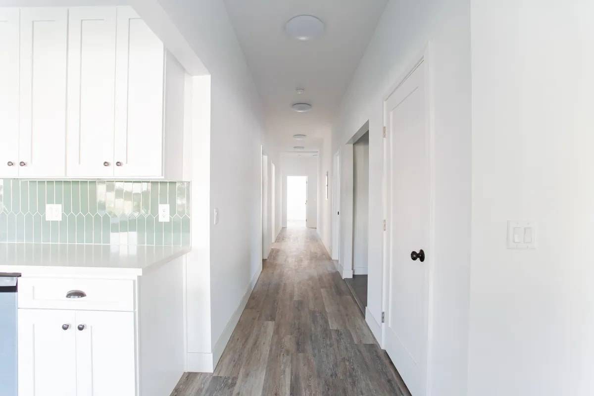 Long bright hallway with white walls, wood-look floors and doors to the bedrooms on either side