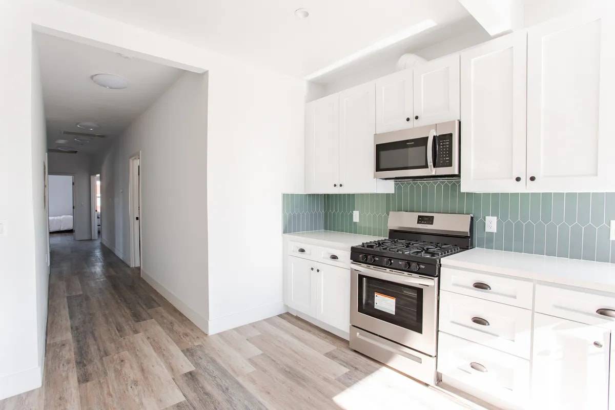 Kitchen corner with a gas range and green tile, opening onto a hallway that leads to the bedrooms